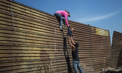 Một gia đình nhập cư trèo qua hàng rào ở biên giới Mỹ - Mexico hồi cuối tháng 11-2018. Ảnh: AFP
