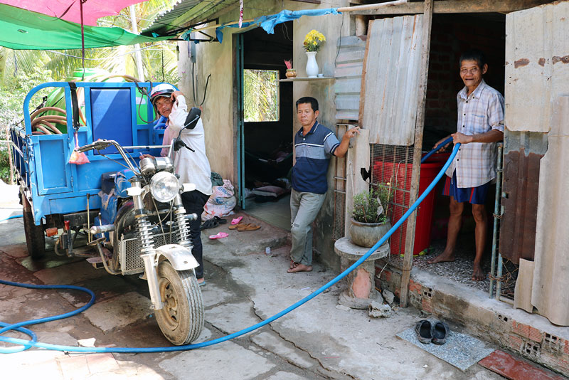 Hộ chính sách neo đơn Nguyễn Văn Mão, 64 tuổi bán vé số (người cầm vòi nước) vui mừng khi nhận nước ngọt miễn phí.