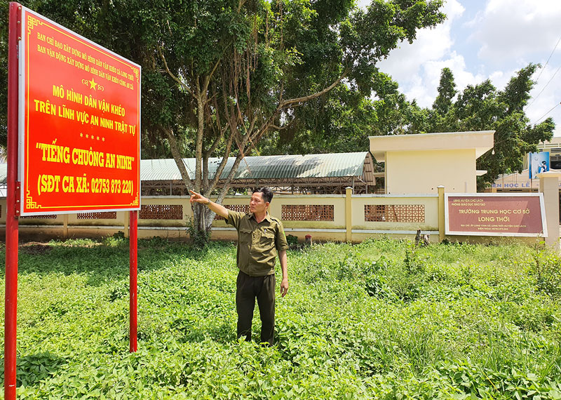 Công an viên xã Long Thới giới thiệu bảng thông tin số điện thoại “Tiếng chuông an ninh” đặt trước khu vực trường học.