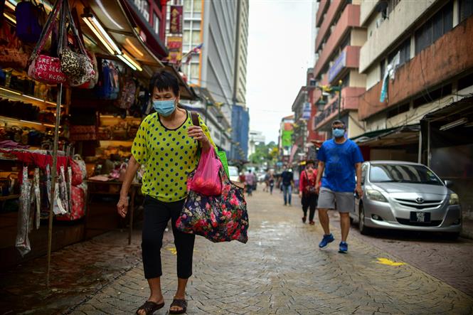 Thế giới gần 15.000 ca tử vong/ngày; 2,3 triệu trẻ em Mỹ mắc bệnh Người dân Malaysia đeo khẩu trang, giãn cách xã hội. Ảnh: AFP/TTXVN