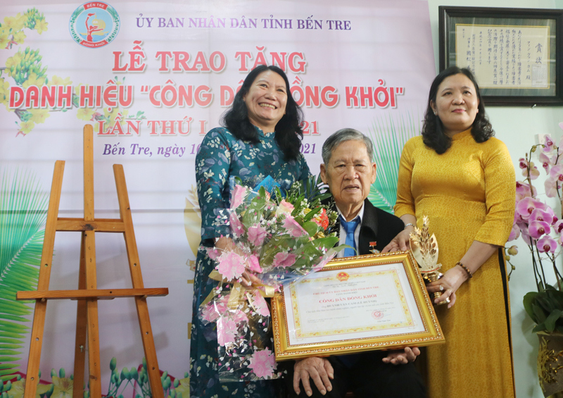 Phó Bí thư Thường trực Tỉnh ủy Hồ Thị Hoàng Yến (bìa phải), Phó Chủ tịch UBND tỉnh Nguyễn Thị Bé Mười (bìa trái) trao hoa và danh hiệu cho ông Huỳnh Văn Cam.