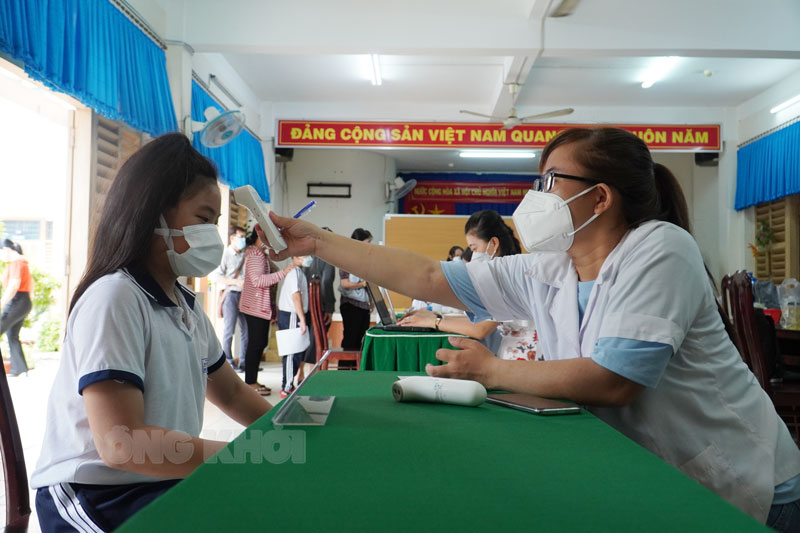 Cán bộ y tế kiểm tra thân nhiệt trẻ dưới 12 tuổi trước tiêm chủng.